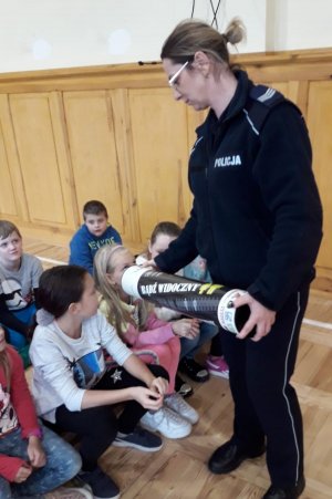 policjantka pokazuje dzieciom tubę promującą noszenie odblasków