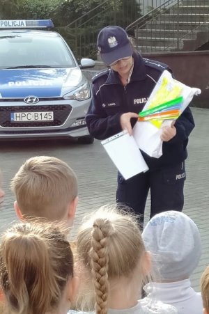 policjantka opowiada dzieciom o bezpieczeństwie na drodze i pokazuje elementy odblaskowe