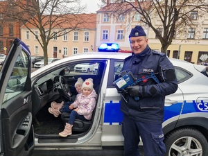 policjant pozuje do zdjęcia z dziećmi, które siedzą w radiowozie